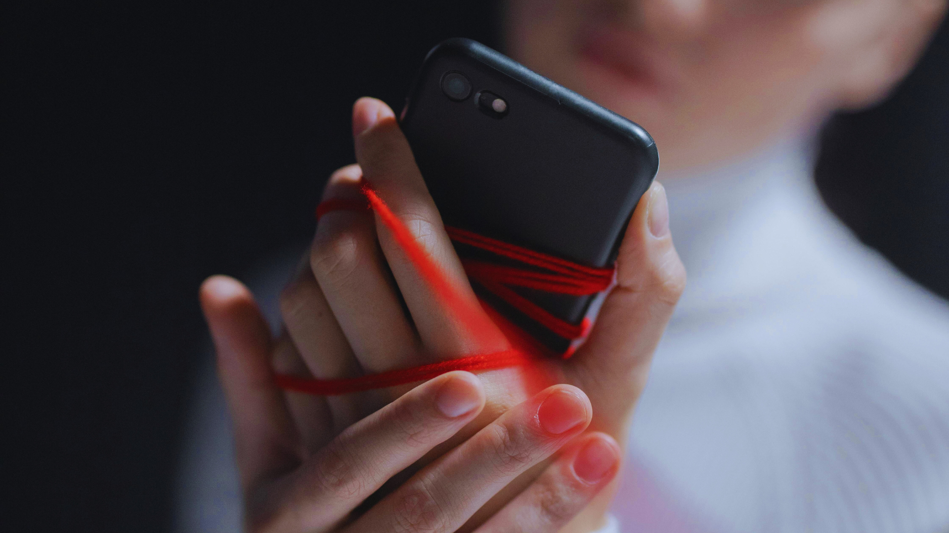 Desconexión digital. Mujer cogiendo un movil envuelta de un cordon que la ata.
